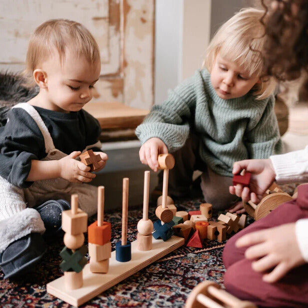 Kinder spielen mit einem Steckspiel aus Holz.